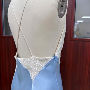 Detailed back view close-up of the gown on a mannequin, showcasing the low-cut open back with crisscross straps and delicate lace triangular insets.