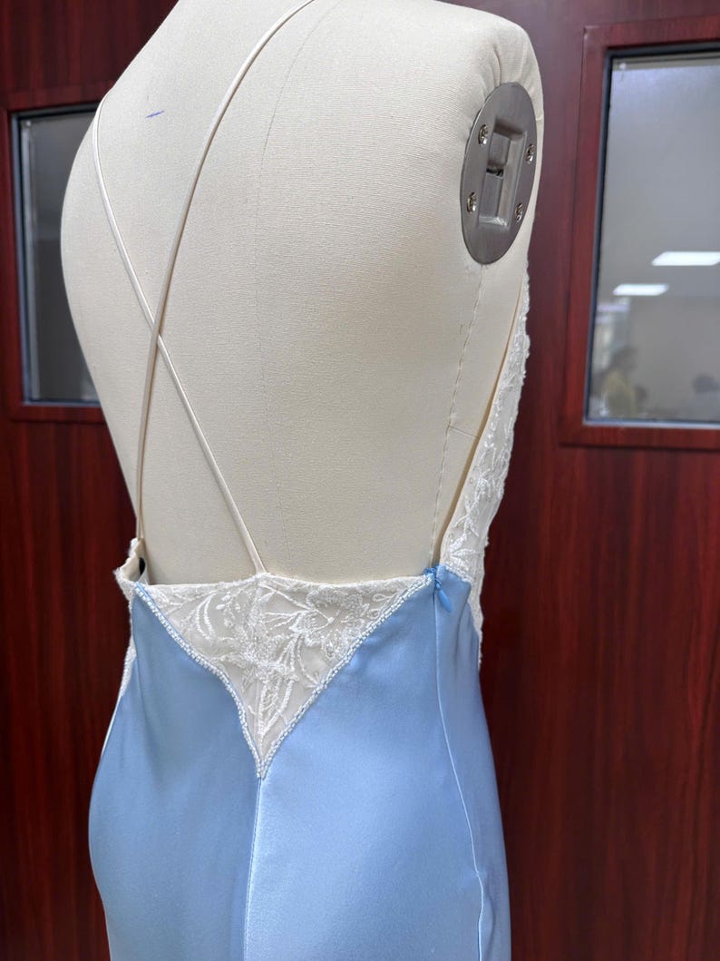 Detailed back view close-up of the gown on a mannequin, showcasing the low-cut open back with crisscross straps and delicate lace triangular insets.