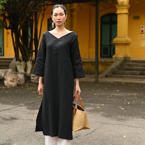 Full-length front shot of the model standing on a paved outdoor pathway, wearing the black V-neck linen tunic and white wide-leg pants.