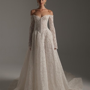 May include: An off-the-shoulder, floor-length gown crafted from intricate white lace. The dress features long, fitted sleeves, a structured bodice with a sweetheart neckline, and a full, voluminous skirt that extends into a train on the floor.