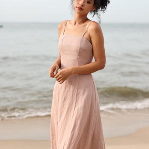 Medium shot from the waist up of a woman looking down thoughtfully, modeling a light mauve line