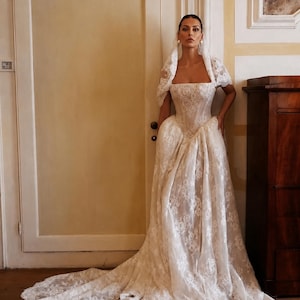 Custom basque waist lace wedding gown with fitted bodice, sheer lace overlay, off-shoulder sleeves, and a cathedral train.