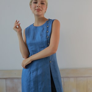 Medium front shot of the model looking into the camera with a gentle smile, emphasizing the textured weave of the organic blue linen fabric and a minimalist fashion style.