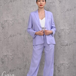 Front view of a model adjusting a lilac natural linen single-breasted jacket, emphasizing its clean two-button front silhouette and casual-chic corporate styling.