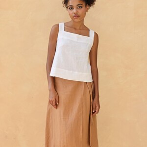 A full-length front studio shot of the model wearing the white sleeveless linen top paired with a light tan wrap midi skirt. The relaxed silhouette highlights the 18.5’’/47cm standard hemline falling neatly over the waistband.