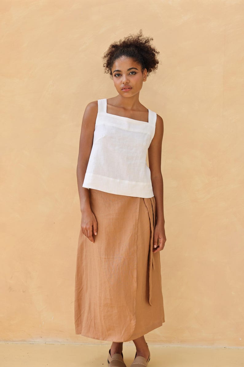 A full-length front studio shot of the model wearing the white sleeveless linen top paired with a light tan wrap midi skirt. The relaxed silhouette highlights the 18.5’’/47cm standard hemline falling neatly over the waistband.