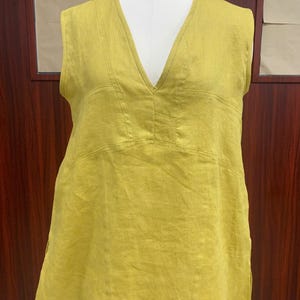 Front view of the chartreuse yellow sleeveless linen tunic displayed on a dress mannequin, highlighting the clean deep V-neckline cut and wide, comfortable armholes.