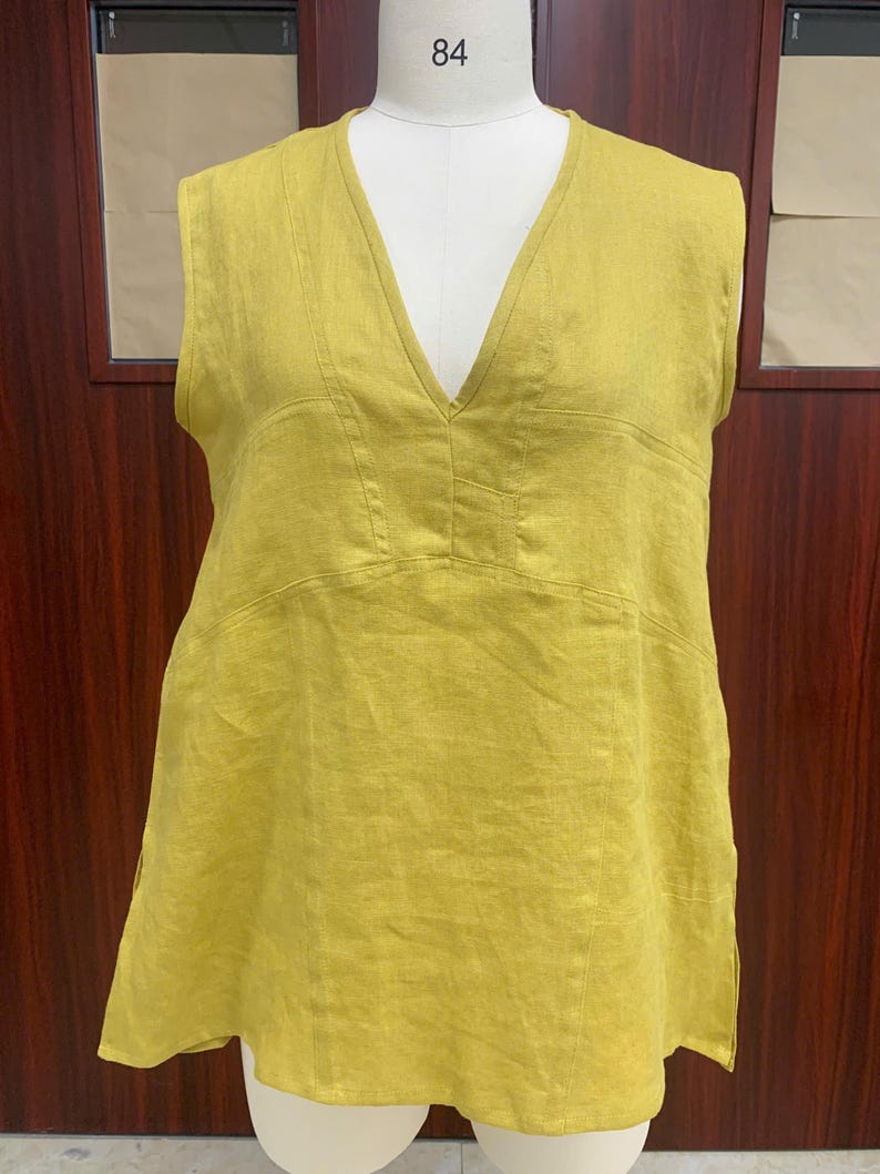 Front view of the chartreuse yellow sleeveless linen tunic displayed on a dress mannequin, highlighting the clean deep V-neckline cut and wide, comfortable armholes.