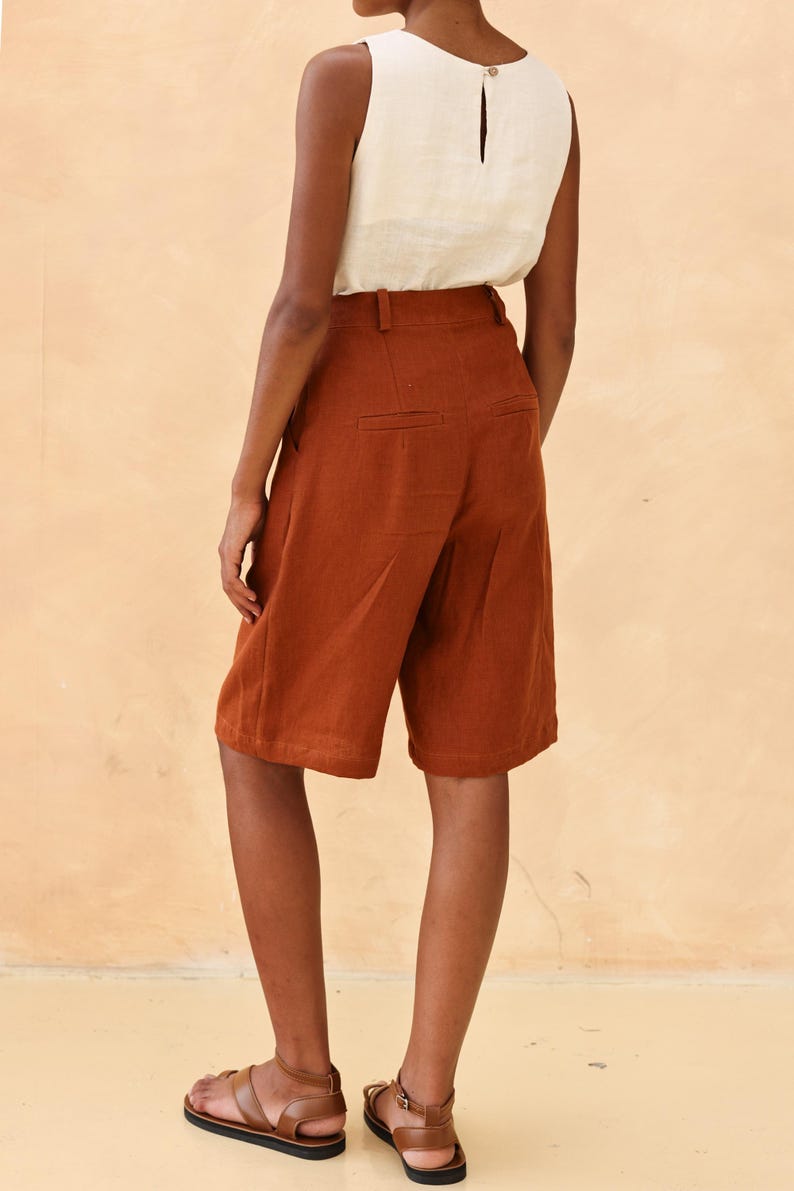 Close-up rear view of the model's lower torso, highlighting the clean tailoring, pocket layout, and structure of the terracotta brown linen shorts or trousers, overlaid with interface editing icons.