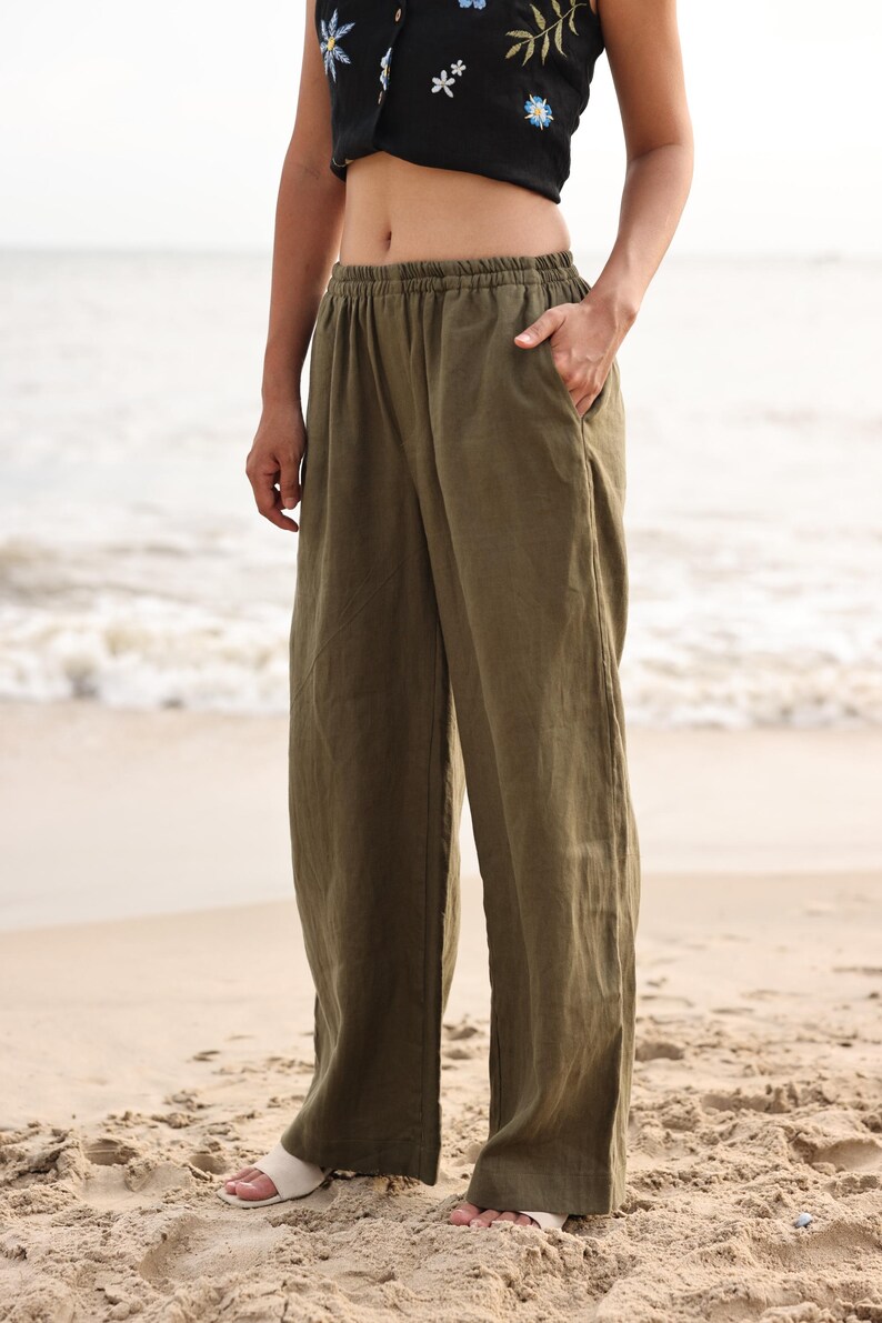 Three-quarter front shot of the model posing with one hand in her pocket on the beach, capturing the modern lifestyle vibe and comfortable versatility of the wide-leg design.