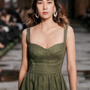 Olive-green linen custom dress with square neckline and full skirt; minimalist wedding guest or bridesmaid style.