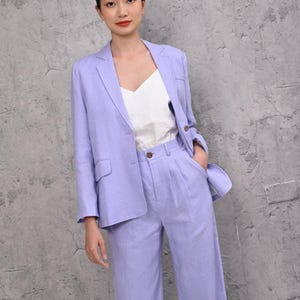 Mid-section shot of a woman modeling a custom-made lilac linen blazer jacket, highlighting the dual statement flap pockets at the waist and clean handcrafted French seams.