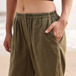 Close-up cropped shot from the waist down focusing on the front side pocket of the olive green linen pants, demonstrating the clean stitch details and functional deep pockets.