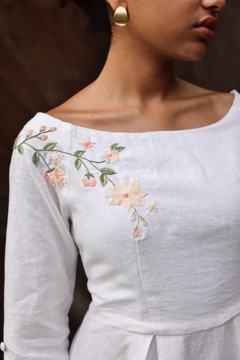A tight close-up shot focusing on the wide boat neckline and chest area. This image perfectly highlights the harmony of the artisanal hand-embroidered floral bouquet on the right shoulder, emphasizing the high-quality craftsmanship and clean finishing of the neckline.