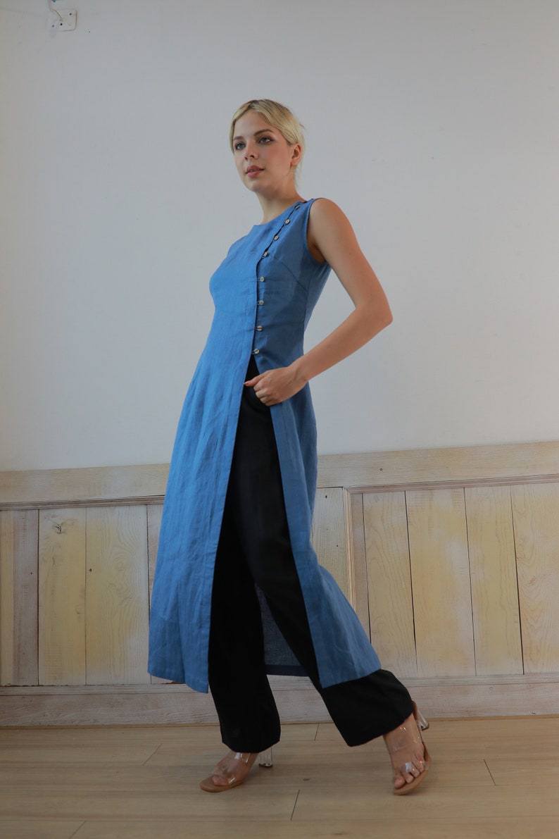 Full-length side view of the model looking slightly downward, demonstrating the dramatic high side slit that creates a modern, layered look with the black trousers.