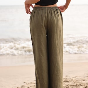 Full-length back view of the model facing towards the ocean, highlighting the smooth fit over the hips and the uniform gathering of the high-rise elasticated waistband.