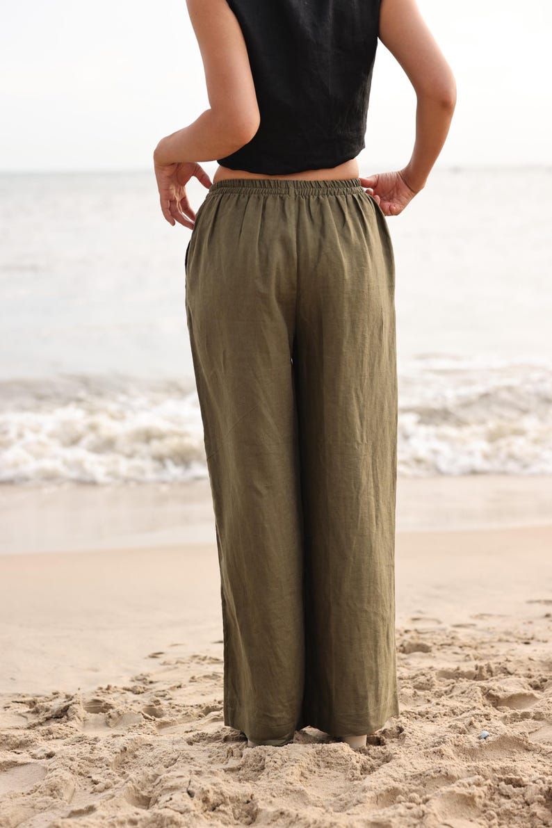 Full-length back view of the model facing towards the ocean, highlighting the smooth fit over the hips and the uniform gathering of the high-rise elasticated waistband.