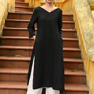 Front full-length shot of the model standing on the terracotta steps, highlighting the minimalist design, comfortable loose fit, and high side slits of the black linen outfit.