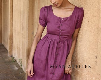 May include: A plum-colored button-down dress with short, puffed sleeves. The dress has a scoop neckline and a fitted waist, with a long skirt that has a front slit. The text "MYAN ATELIER" is printed on the bottom right of the dress.