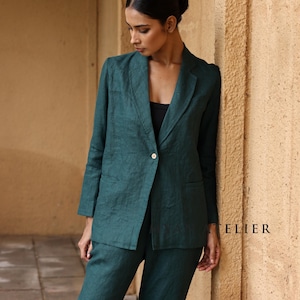 May include: A teal green blazer and matching pants suit. The blazer has a single button closure and two front pockets. The suit is made of a textured fabric. The word "ATELIER" is printed on the right side of the image.