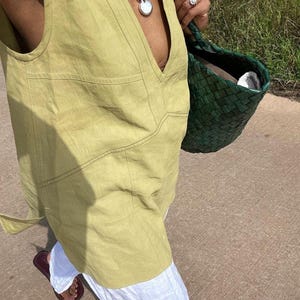 Side-angle shot of the person walking outdoors, capturing the relaxed fit, slightly longer hemline, and breathable natural texture of the chartreuse yellow sleeveless top.