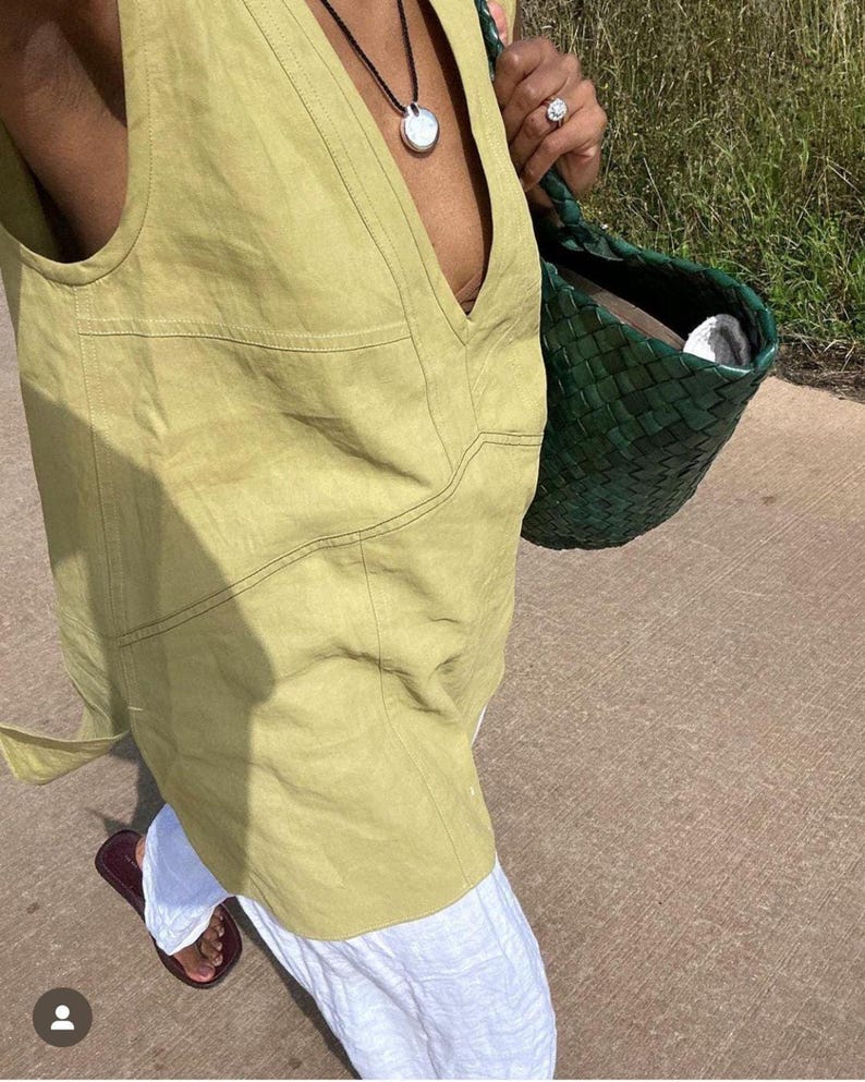 Side-angle shot of the person walking outdoors, capturing the relaxed fit, slightly longer hemline, and breathable natural texture of the chartreuse yellow sleeveless top.