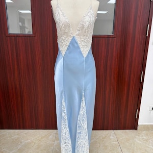 Full-length front view of the light blue silk-blend satin slip dress on a mannequin, showcasing the intricate white lace insets and high thigh slit.