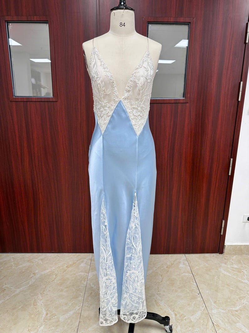 Full-length front view of the light blue silk-blend satin slip dress on a mannequin, showcasing the intricate white lace insets and high thigh slit.