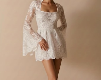 May include: A white lace mini dress with long, flared sleeves and a square neckline. The dress features intricate floral lace detailing and a fitted bodice that flares into a short skirt. A matching lace bolero completes the ensemble.