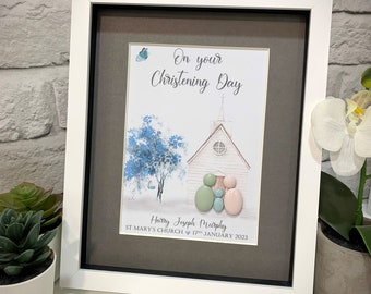 Könnte beinhalten: Ein gerahmter Druck mit einer Aquarell-Illustration einer Kirche, eines Baumes und einer dreiköpfigen Familie, die durch bemalte Kieselsteine dargestellt wird. Der Text lautet "On your Christening Day", "Harry Joseph Murphy", "St. Mary's Church" und "17th January 2023".