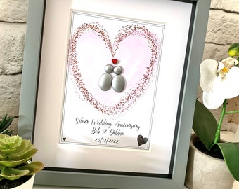 May include: A framed picture with a heart made of glitter and two gray pebble figures inside. The text below reads "Silver Wedding Anniversary Bob & Debbie 23/12/2022".