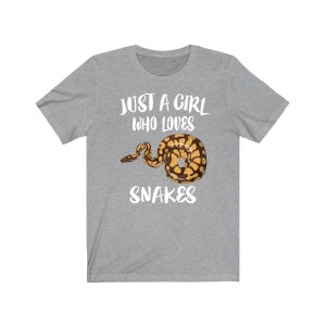 Könnte beinhalten: Ein graues T-Shirt mit dem Text "Just a girl who loves snakes" und einer Grafik einer braunen und gelben Schlange.