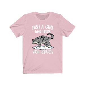 May include: Pink t-shirt with a white graphic of a snow leopard and the text "Just a girl who loves snow leopards".