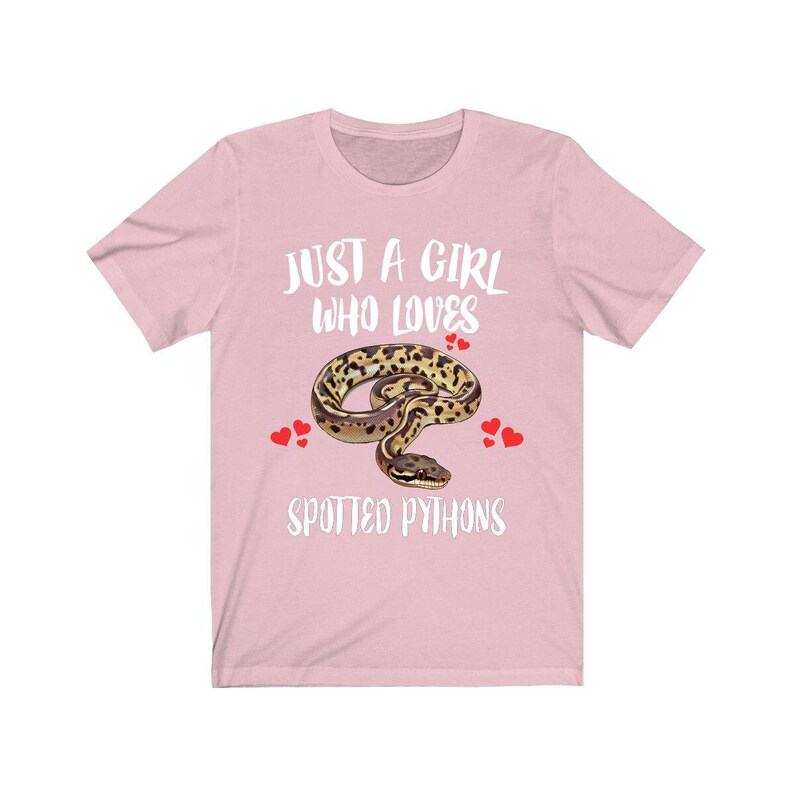 May include: A light pink t-shirt with the text "JUST A GIRL WHO LOVES SPOTTED PYTHONS" in white. The shirt features a graphic of a spotted python and red heart accents.