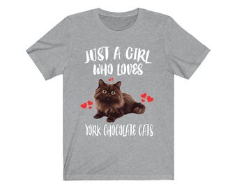 May include: A heather gray t-shirt with the text "JUST A GIRL WHO LOVES YORK CHOCOLATE CATS." The shirt features a brown cat illustration with red heart accents. The design is printed on a short-sleeved crew neck tee.