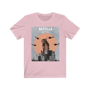 May include: Pink t-shirt with a graphic of a giant rat standing on a city skyline. The graphic says "RATZILLA" and "ねずみ" in Japanese.