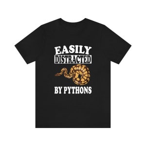 May include: Black t-shirt with white text that reads "Easily Distracted By Pythons". A brown and yellow python is pictured below the text.