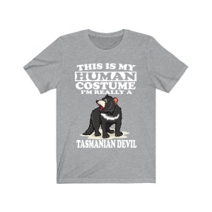 May include: A grey t-shirt with the text "THIS IS MY HUMAN COSTUME I'M REALLY A TASMANIAN DEVIL" in white. The shirt features a cartoon illustration of a Tasmanian Devil.