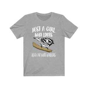 May include: A grey t-shirt with a black and white warbler illustration on a branch. The text reads "JUST A GIRL WHO LOVES BLACK AND WHITE WARBLERS". A casual tee for bird enthusiasts.
