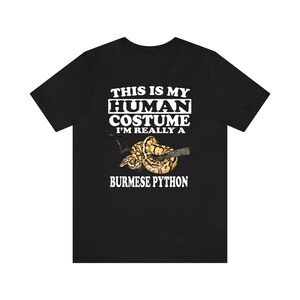 Könnte beinhalten: Schwarzes T-Shirt mit weißem Text, der "This is my human costume I'm really a Burmese Python" lautet. Ein gelber und brauner Birmanischer Python ist auf dem T-Shirt abgebildet.