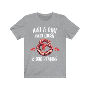 Könnte beinhalten: Ein graues T-Shirt mit dem Text "JUST A GIRL WHO LOVES BLOOD PYTHONS". Das Shirt zeigt eine Grafik einer rot-braunen Schlange mit roten Herzen auf beiden Seiten. Das Shirt hat einen Rundhalsausschnitt.