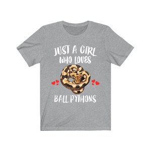 K&ouml;nnte beinhalten: Graues T-Shirt mit dem wei&szlig;en Text "JUST A GIRL WHO LOVES BALL PYTHONS". Das Shirt zeigt eine Grafik einer K&ouml;nigspython mit roten Herzakzenten.
