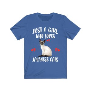 Puede incluir: Camiseta azul con el texto blanco "JUST A GIRL WHO LOVES JAVANESE CATS". Una ilustración de un gato siamés está centrada debajo del texto, con gráficos de corazones rojos.