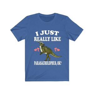 May include: A blue t-shirt with the text "I just really like Parasaurolophus, ok?" in white. A cartoon Parasaurolophus dinosaur is in the centre of the shirt with pink hearts around it.