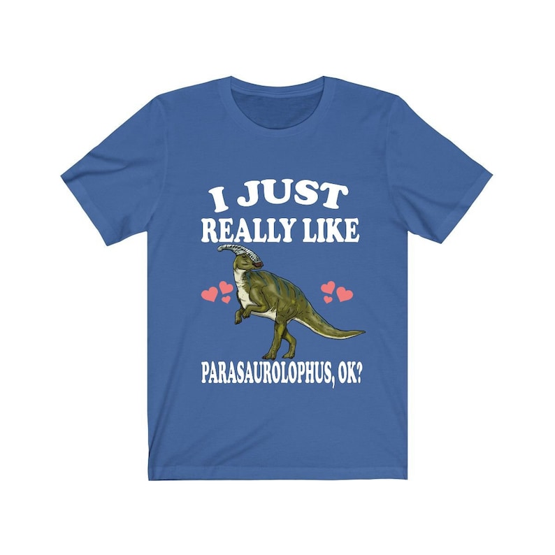 May include: A blue t-shirt with the text "I just really like Parasaurolophus, ok?" in white. A cartoon Parasaurolophus dinosaur is in the centre of the shirt with pink hearts around it.