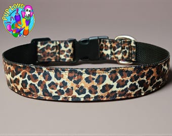 May include: A dog collar with a leopard print design. The collar features a black buckle and a metal D-ring. The background is a solid color. The collar is approximately 1 inch wide.