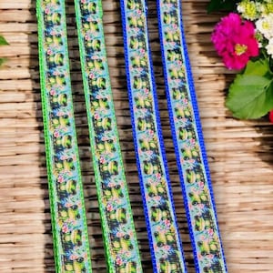 May include: Four dog leashes with a repeating pattern of green frogs and pink flowers on a light blue background. Two leashes are trimmed in green, and two are trimmed in blue. Each leash has a silver clasp and a silver ring.