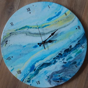 Könnte beinhalten: Eine runde Uhr mit römischen Ziffern auf einem abstrakten blauen, weißen und gelben Hintergrund. Die Uhrzeiger sind schwarz.