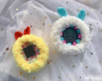 May include: Two crocheted plush toy covers for a digital pet device. One is white with blue bunny ears and the other is yellow with red bunny ears.