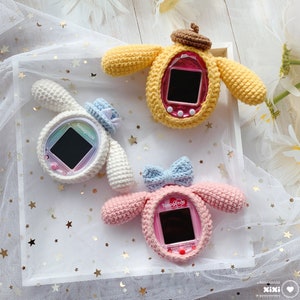 Può includere: Tre giocattoli di peluche a forma di cane, realizzati a uncinetto, ognuno con uno schermo e pulsanti di colore diverso. I giocattoli sono su uno sfondo bianco con stelle dorate.